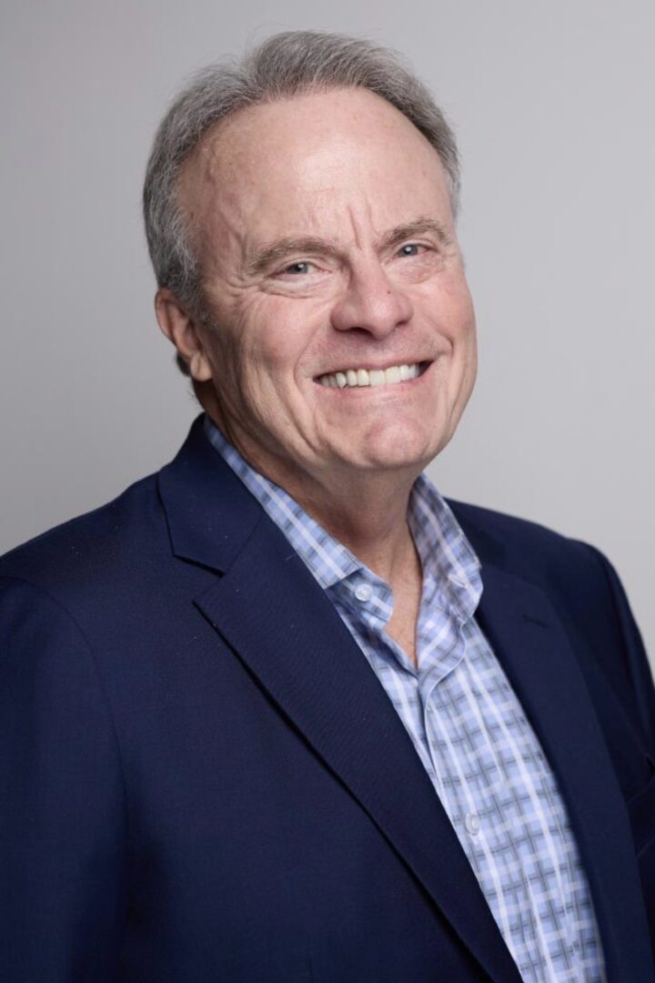 Smiling man in suit and checkered shirt.